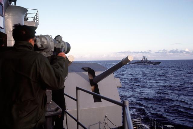 crewman aboard the USS IOWA (BB-61) uses the ship's binoculars to observe the Soviet Krivak I class guided missile frigate ZHARKYY as it operates near the battleship..jpg